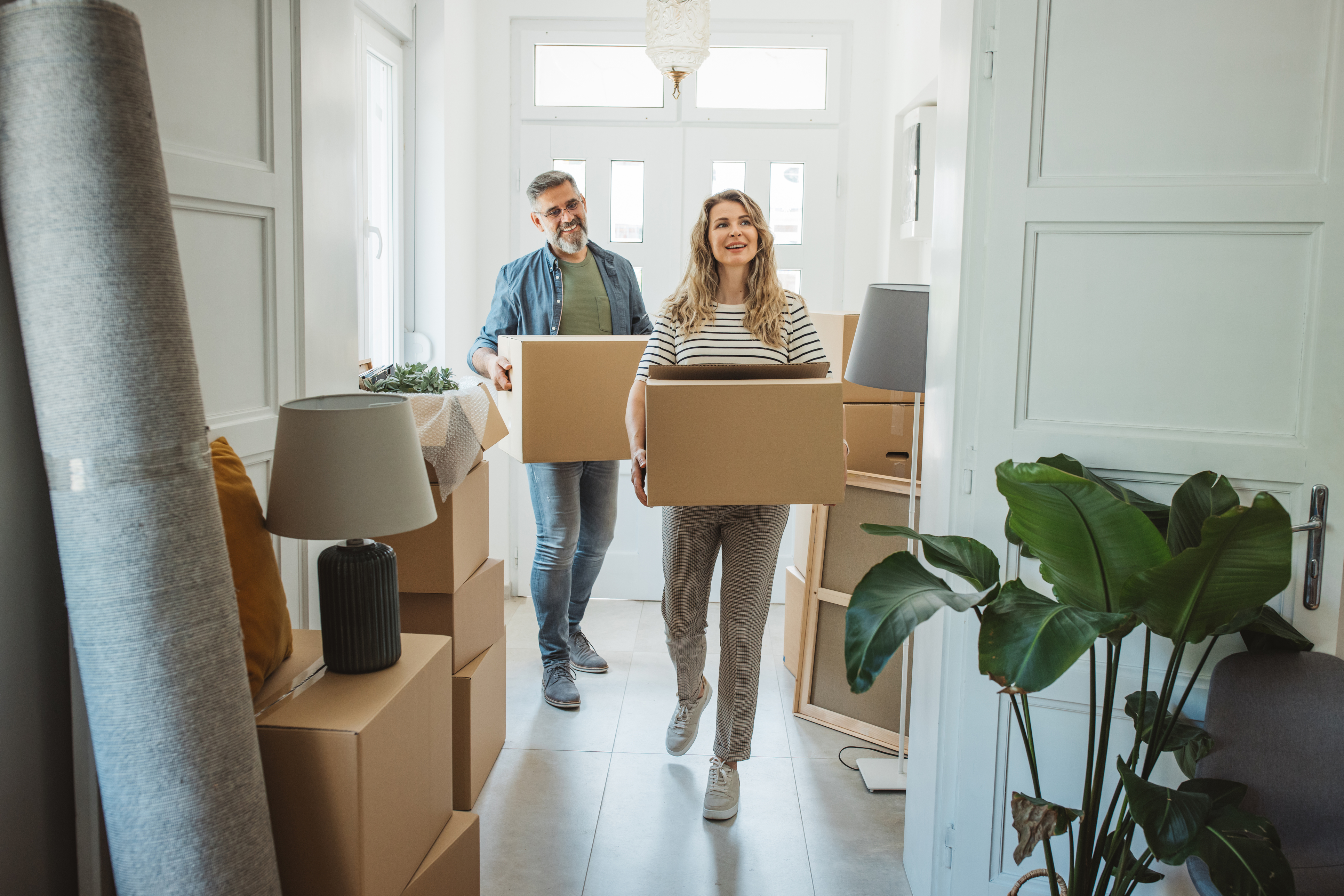 Couple carrying moving boxes into a bright home
